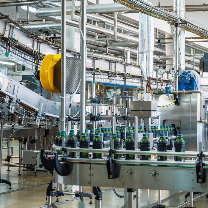 Conveyor belt or line in beverage plant with modern automated industrial machine equipment. Plastic PET bottles in factory interior.